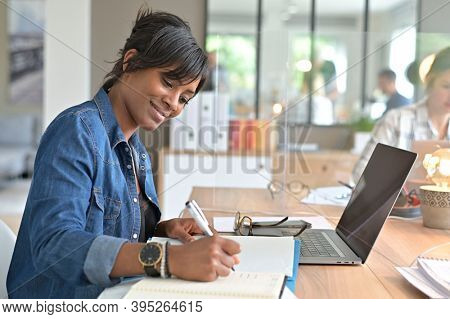 Office worker woman in open space area, protected by plexiglas