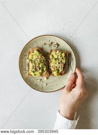 Female Hand Hold A Green Plate Withy Avocado Toasts With Sprouts And Various Seeds. Top View. Copy S