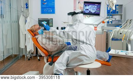 Dentist Assistant In Potective Suit Measuring Patient Temperature Before Dental Examination During C