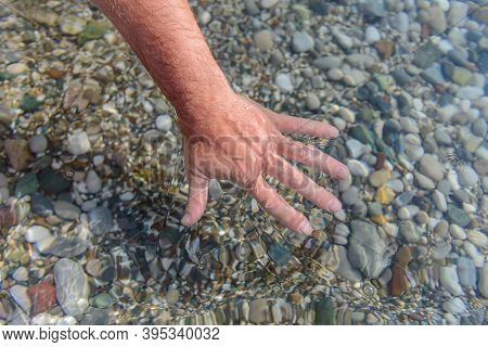 Water. Hand. Man\'s hand touching a natural water source. Top view. Sea water through which you can see the stones lying on the bottom.