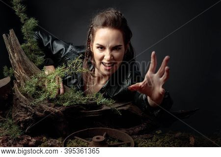 A Young Woman In A Black Leather Jacket Climbs Out Of The Pit Holding On To A Snag. Angry Girl Stret