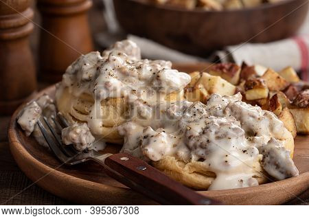 Closeup Of Biscuits With Creamy Sausage Gravy And Fried Potatoes On A Wooden Plate