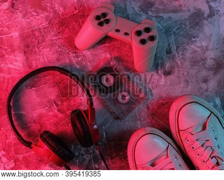 Wired Headphones, Sneakers, Audio Cassette, Gampad On Concrete Background. Neon Blue-red Gradient Li