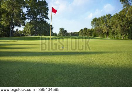 Low Angle View Of A Golf Green With Red Flag And Ball On A Sunny Afternoon