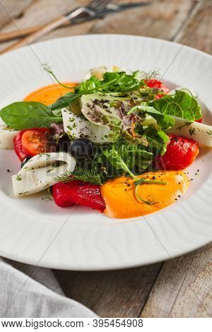 Roasted pepper salad with calamari and fresh greens. Rustic wooden table and grey textile