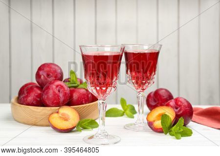 Delicious Plum Liquor, Ripe Fruits And Mint On Table Against White Background. Homemade Strong Alcoh
