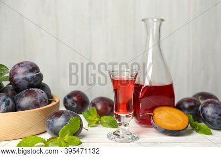 Delicious Plum Liquor, Ripe Fruits And Mint On White Wooden Table. Homemade Strong Alcoholic Beverag
