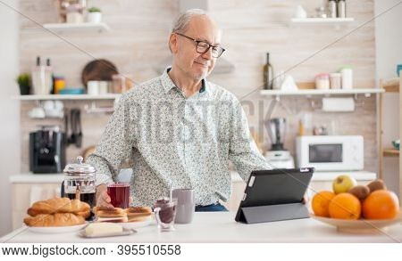 Senior Person Browsing On Tablet Pc In Kitchen During Breakfast Having A Healthy Lifestyle. Elderly 