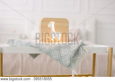 Front View Of Wooden Night Lamp With Giraffe Cut Out Picture, On Gray Blanket At Cozy Light Bedroom 