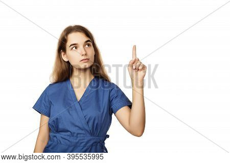 Young Beautiful Female Doctor In A Blue Surgical Gown Shows A Finger To The Side Isolated On A White