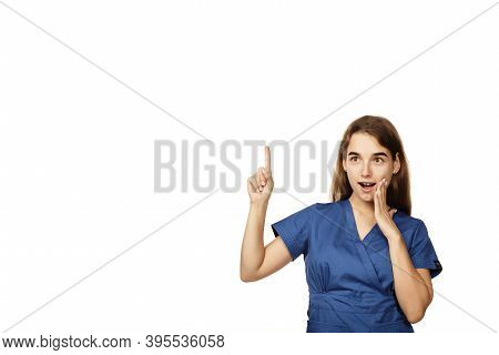 Young Beautiful Female Doctor In A Blue Surgical Gown Shows A Finger To The Side Isolated On A White