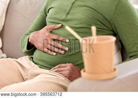 consumption and people concept - close up of overeaten man and cup of takeaway food at home