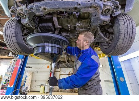 Happy Car Mechanic Changes Oil In A Workshop. Mechanic Standing Under The Car And Draining Oil Into 