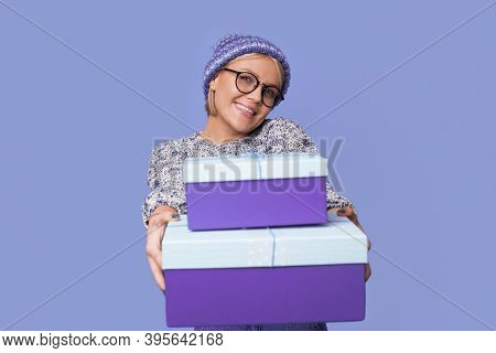 Charming Blonde Woman Is Smiling At Camera And Giving A Present While Wearing Knitted Sweater And Ha