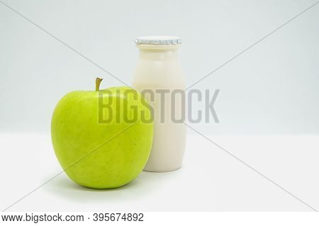 Natural liquid yogurt with probiotics in small plastic bottle and green apple on white background. Healthy, balanced diet food, healthy breakfast. Space for text.