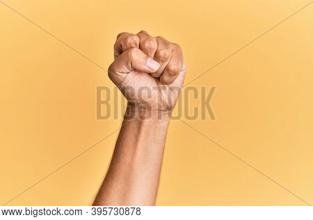 Arm and hand of caucasian man over yellow isolated background doing protest and revolution gesture, fist expressing force and power 