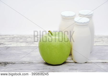 Natural Liquid Yogurt With Probiotics In Small Plastic Bottles And Yellow Apple On Wood Table. Healt