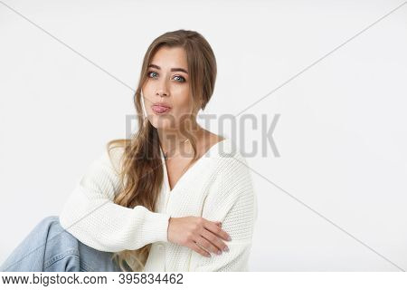 Beautiful Young And Funny Woman In A Blue Jeans And White Sweater Sitting On A White Background. Por