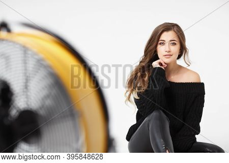 Pretty Young Woman In A Black Leather Leggings And Black Sweater Sitting On A White Background. A Ca