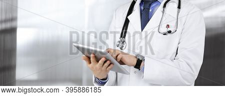 Unknown Male Doctor Iusing Tablet Computer In His Hands, While Standing In Clinic. Medicine Concept 
