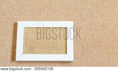 White Pciture Frame Blank On The Eco Friendly Textured Burlap Fabric. Mock Up Photo, Space For Your 