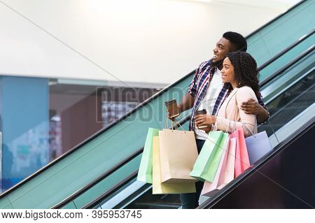 Happy African American Couple Riding Escalator In Shopping Mall, Enjoying Making Purchases Together,