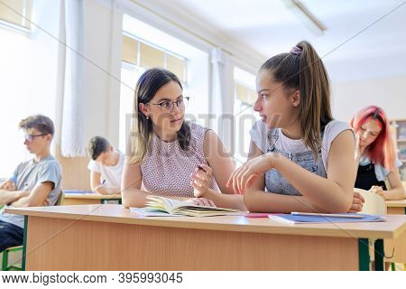 Young Woman Teacher Teaches Lesson In Classroom Of Teenage Children, Teacher Sits At Desk With Stude