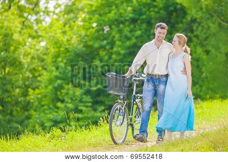 Young Caucasian Couple Having A Stroll In Park With Bike
