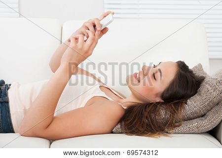 Woman Using Mobile Phone While Lying On Sofa