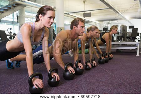 Fitness class in plank position with kettlebells at the gym