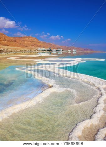 The path from salt picturesquely curls in salty water. Hotels are reflected in smooth water ashore. Israeli coast of the Dead Sea