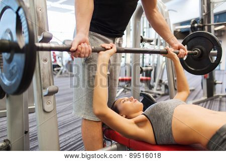 sport, fitness, teamwork, weightlifting and people concept - young woman and personal trainer with barbell flexing muscles in gym