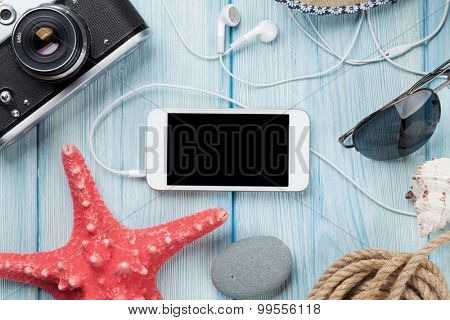 Smartphone and camera on wooden table with starfish and shells. Top view with copy space