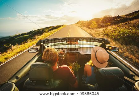 Happy Young Couple Driving Along Country Road in Convertible at Sunset