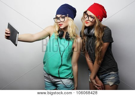 two hipster girls friends taking selfie with digital tablet, studio shot over gray vackground