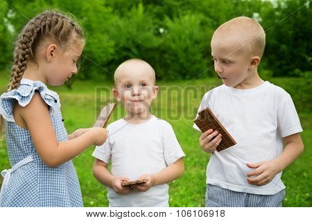 Happychildren eating chocolate bars outdoors in summer park