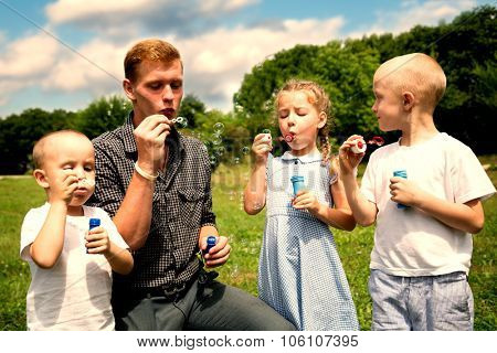 Elder brother teaches the younger brothers and sister blowing bubbles. Retro vintage  filter effect.