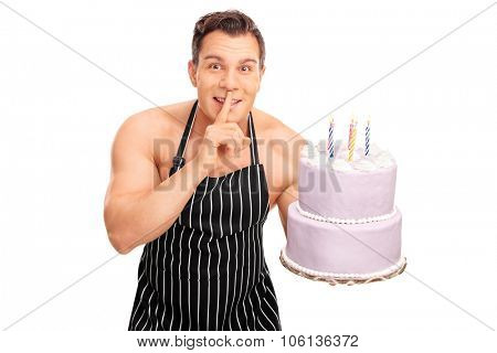 Naked chef with a black apron holding a birthday cake and gesturing silence with finger on his lips isolated on white background