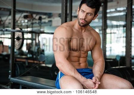 Portrait of a thoughtful fitness man resting on the bench in gym