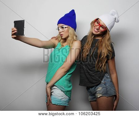 two hipster girls friends taking selfie with digital tablet, studio shot over gray vackground