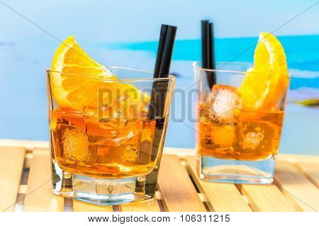 Two Glasses Of Spritz Aperitif Aperol Cocktail With Orange Slices And Ice Cubes On Blur Beach Backgr