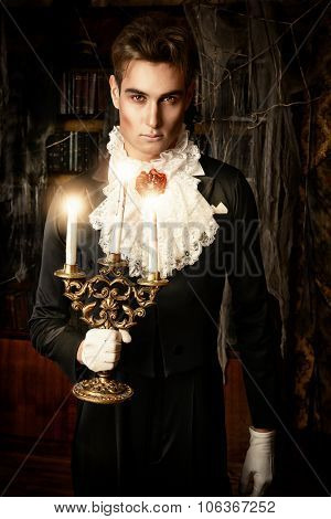 Handsome vampire man wearing elegant tailcoat stands in the old medieval castle. Halloween.