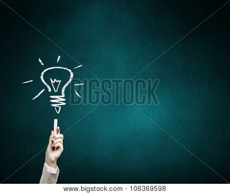 Human hand darwing light bulb as idea concept with chalk