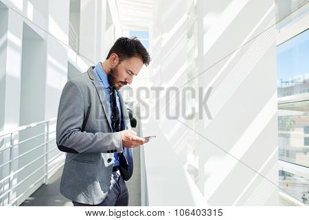 Young smart male entrepreneur reading something on cell telephone during break