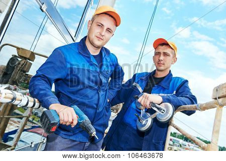 Portrait of two builders worker with glass suction plate and hand drill in front of facing wall of business building
