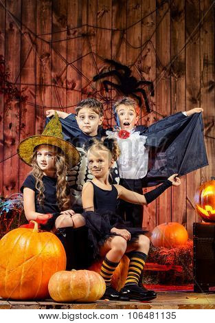 Cheerful children in halloween costumes celebrating halloween in a wooden barn with pumpkins. Halloween concept.