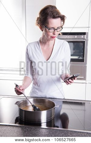 Attractive Woman In Modern Ktchen Cooking And Looking On The Phone