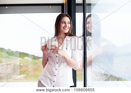 beautiful young woman drink first morning coffee at modern home interior with rain drops on big window door glass