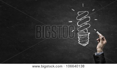 Human hand darwing light bulb as idea concept with chalk