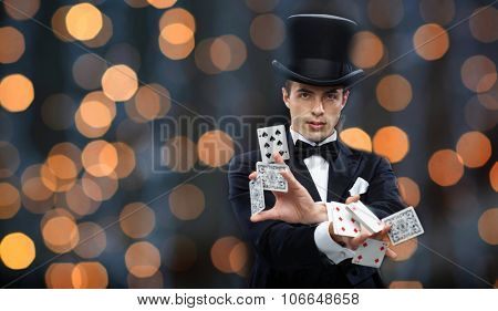 magic, gambling, casino, people and show concept - magician in top hat showing trick with playing cards over nigh lights background